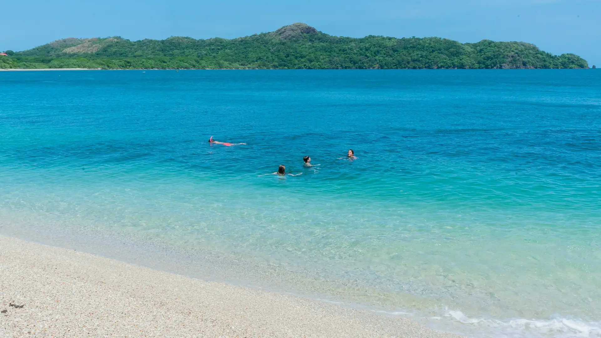 Swimmers floating in clear turquoise water near a white-sand beach